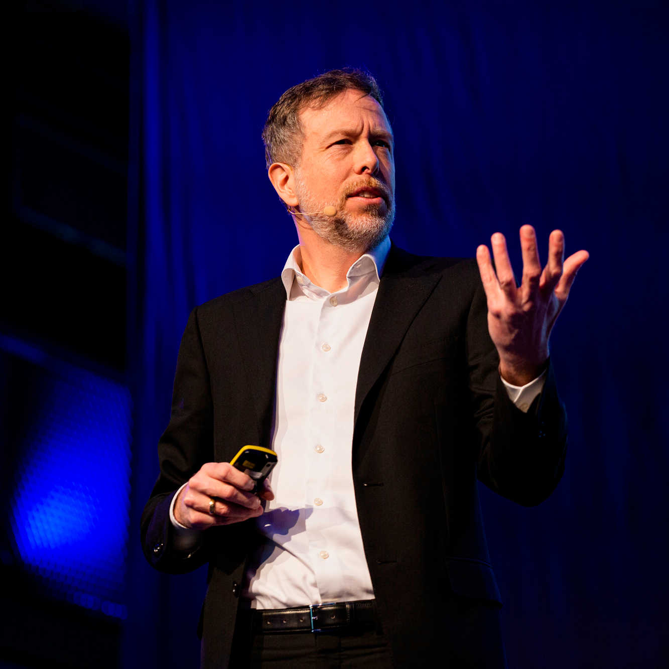 Keynote-Speaker Dr. Nicolas Dierks auf der Bühne beim Vortrag, eine Hand offen vor sich bei der Erläuterung eines inspirierenden Gedankens.